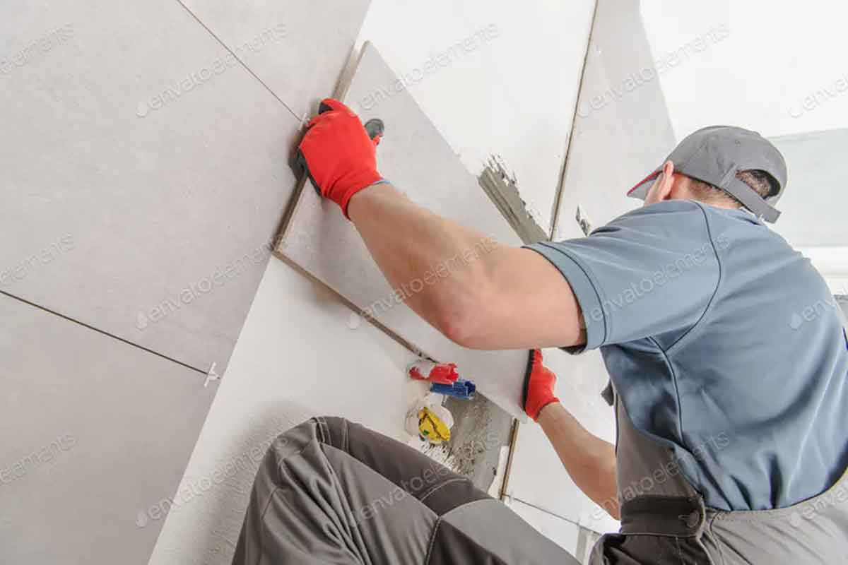 a man squatting, fixing wall tiles